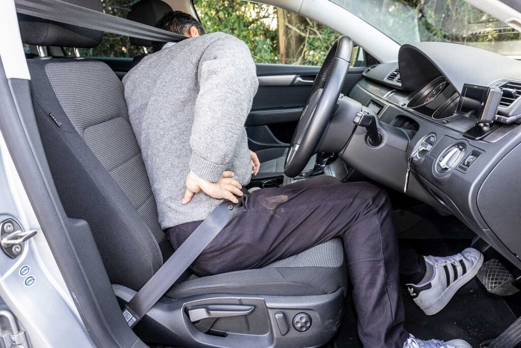 運転中に腰の痛みを打って得ている男性ドライバーの写真。