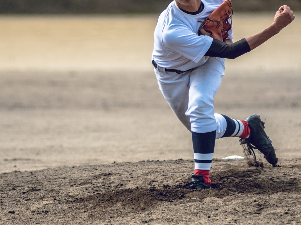 野球の試合でピッチャーとしてボールを投げている高校生の写真。