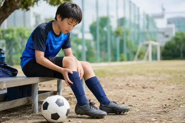 膝の痛みでサッカーができずに困っている男の子の写真。